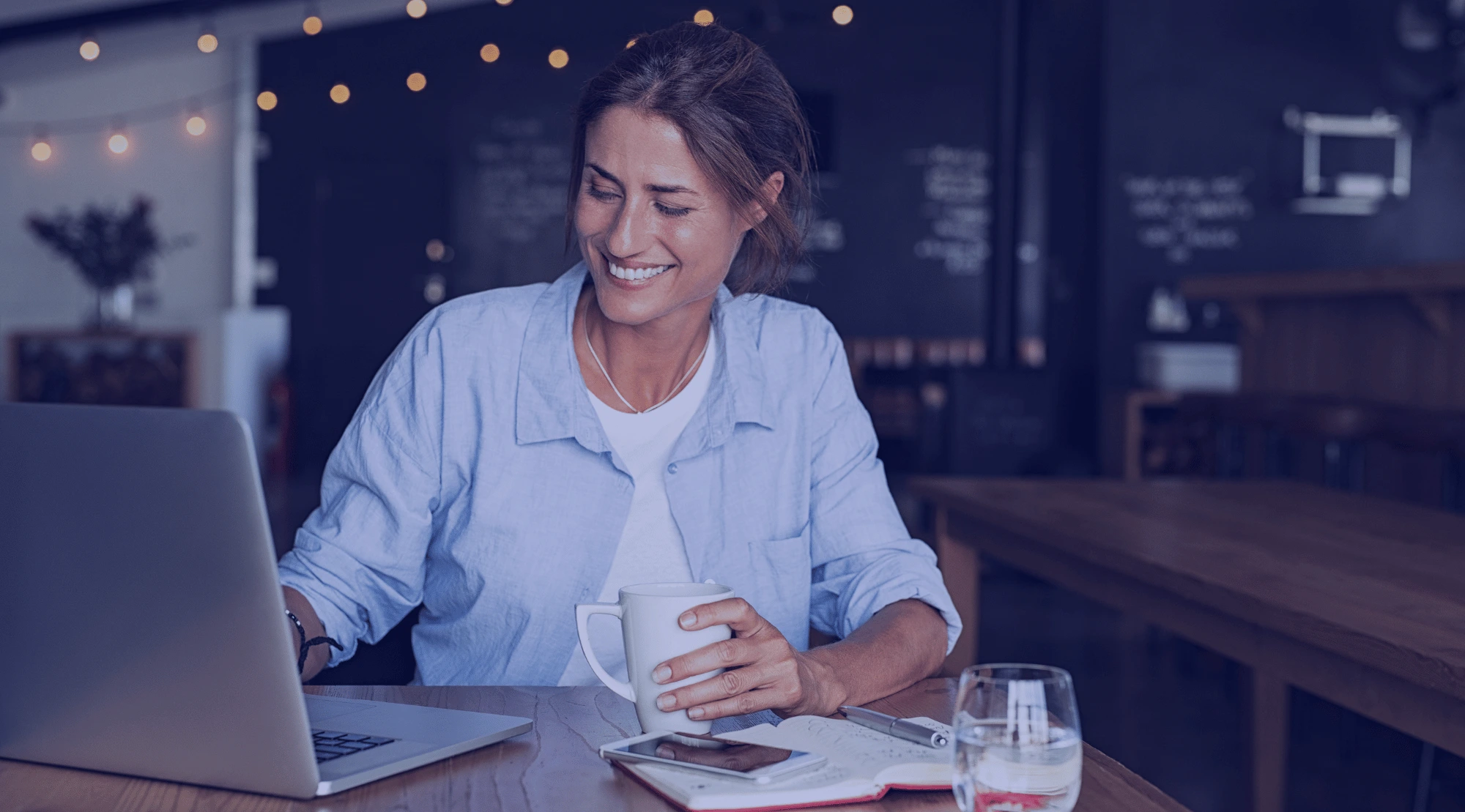 Frau arbeitet lächelnd mit einer Tasse Kaffee an ihrem Laptop.